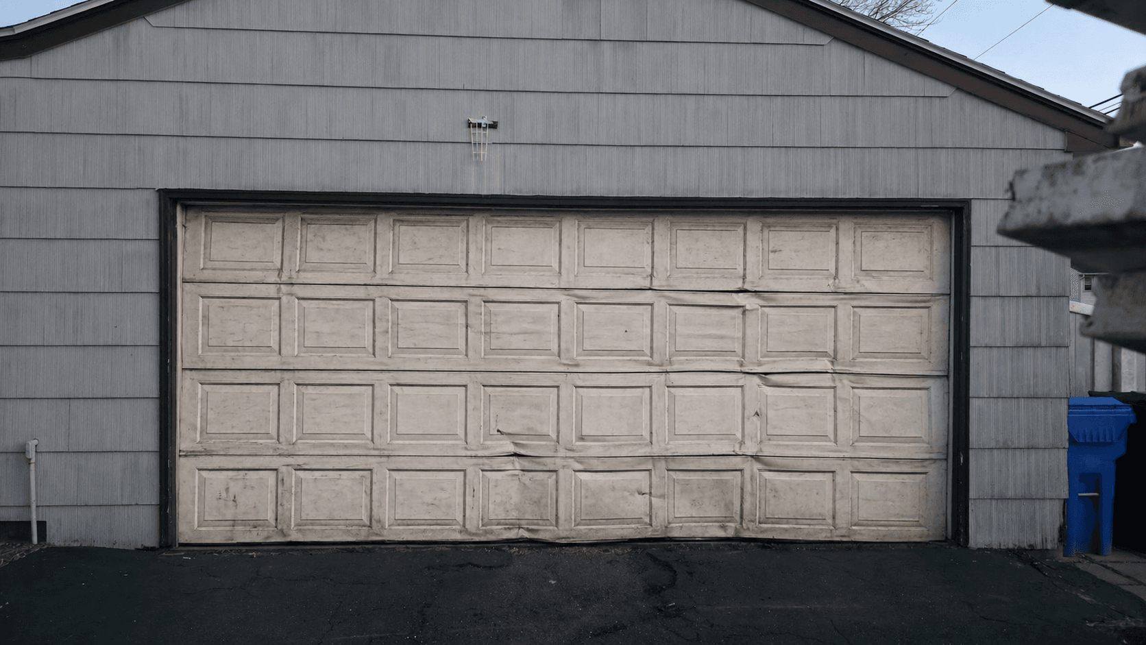 Aging double garage door with dents and sagging panels before replacement