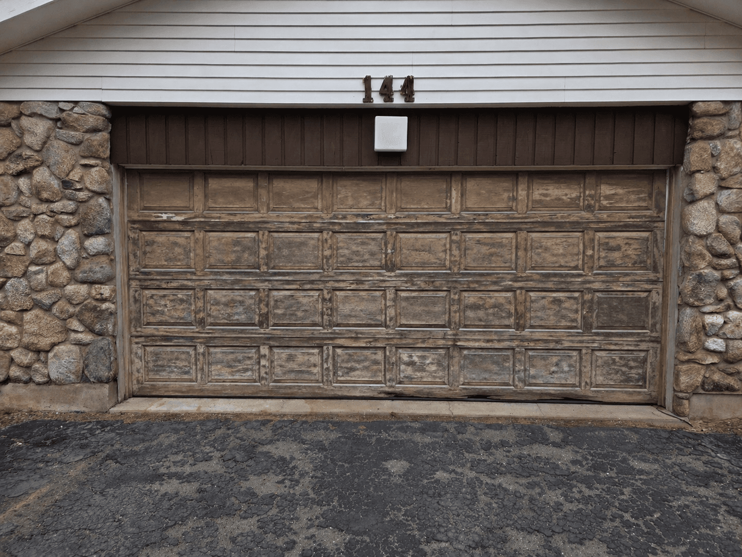 Weathered wood-tone double garage door with peeling finish before replacement