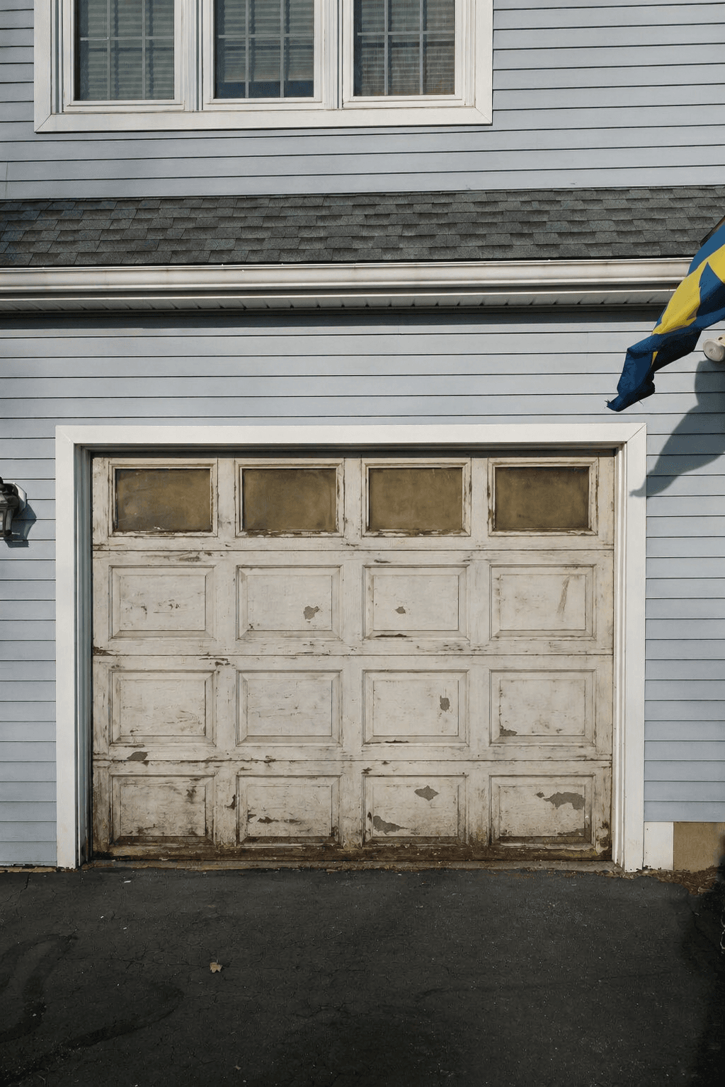 Old single garage door with peeling paint and clouded windows before replacement