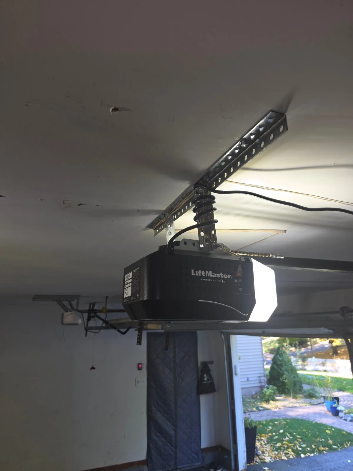A new LiftMaster garage door opener mounted to a metal ceiling bracket with its light illuminated inside a garage in Glastonbury, CT.