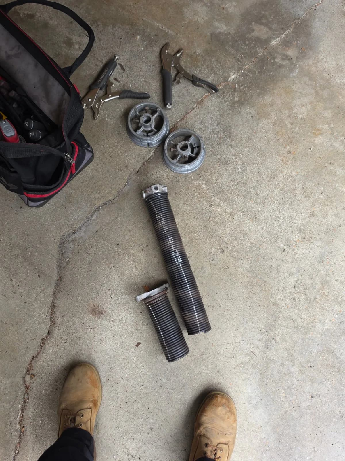 Broken garage door torsion spring pieces, cable drums, and pliers lying on a concrete garage floor.