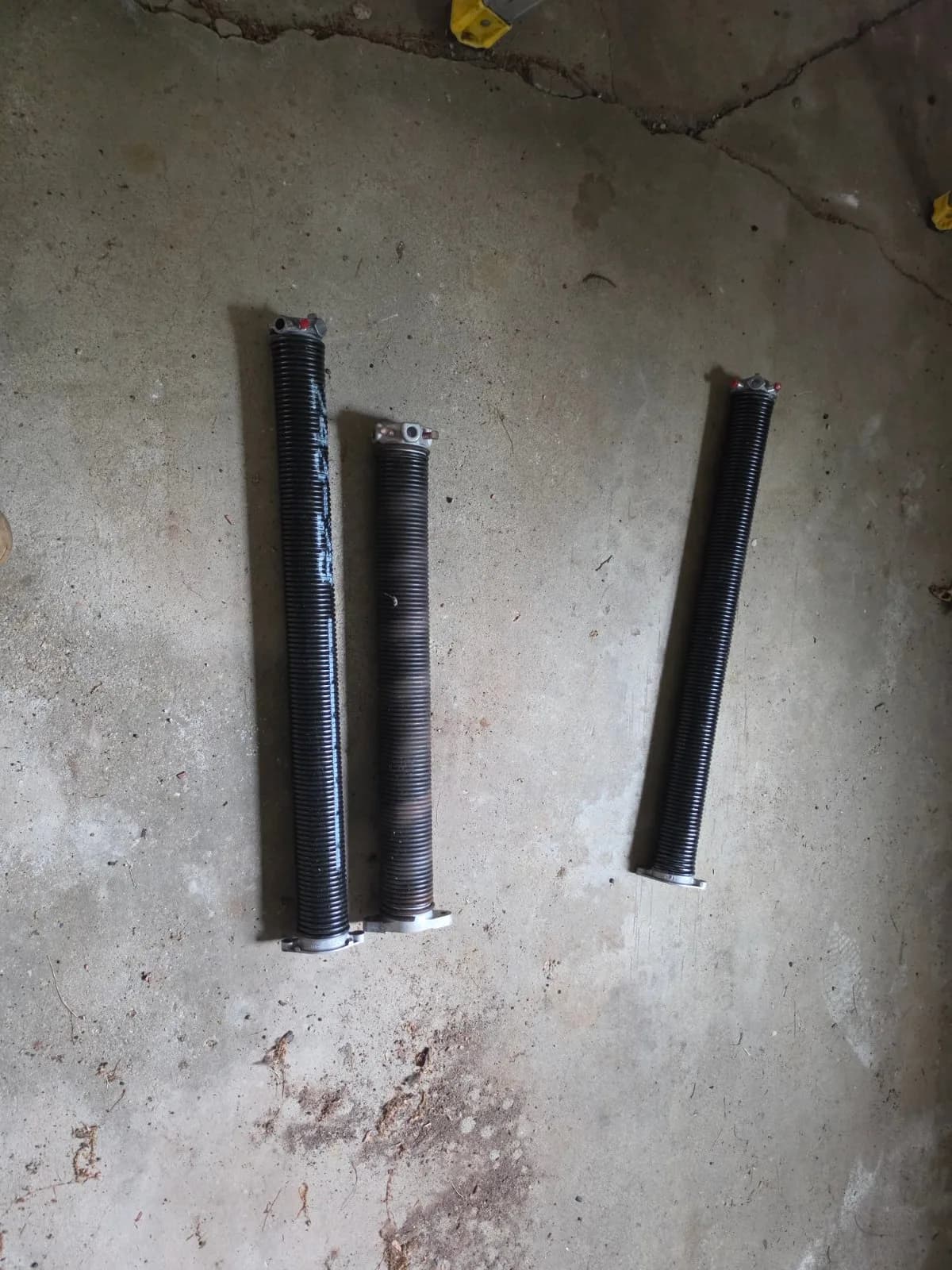 Three garage door torsion springs laid out side by side on a concrete floor.