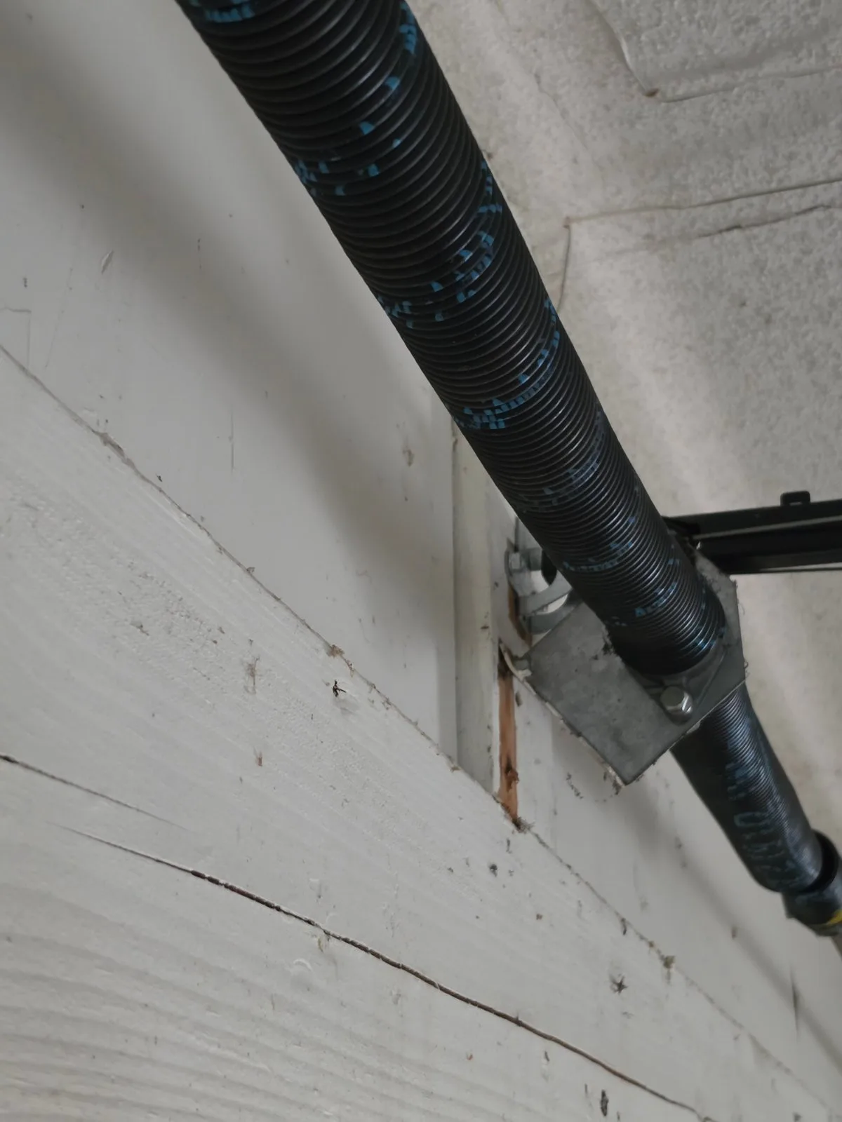Close-up of a garage door torsion spring and center bracket mounted on a wooden header.