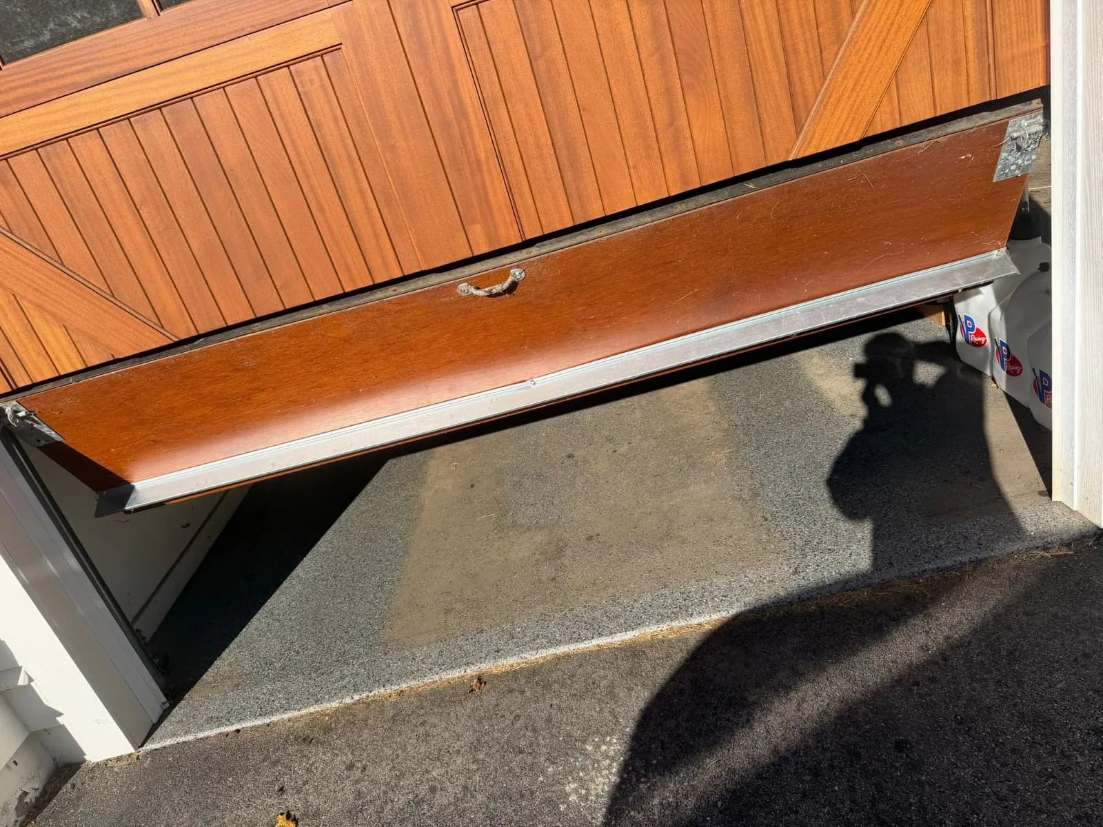 Bottom section of an off-track wooden garage door hanging unevenly above the garage floor in Avon, CT.