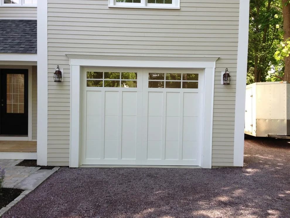A closed white carriage-house style garage door with top window panes on a light grey sided house in Berlin, CT.