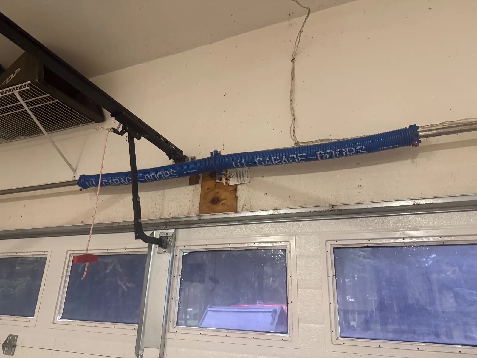 Blue high-cycle garage door torsion springs installed on the torsion shaft above a white garage door with windows.