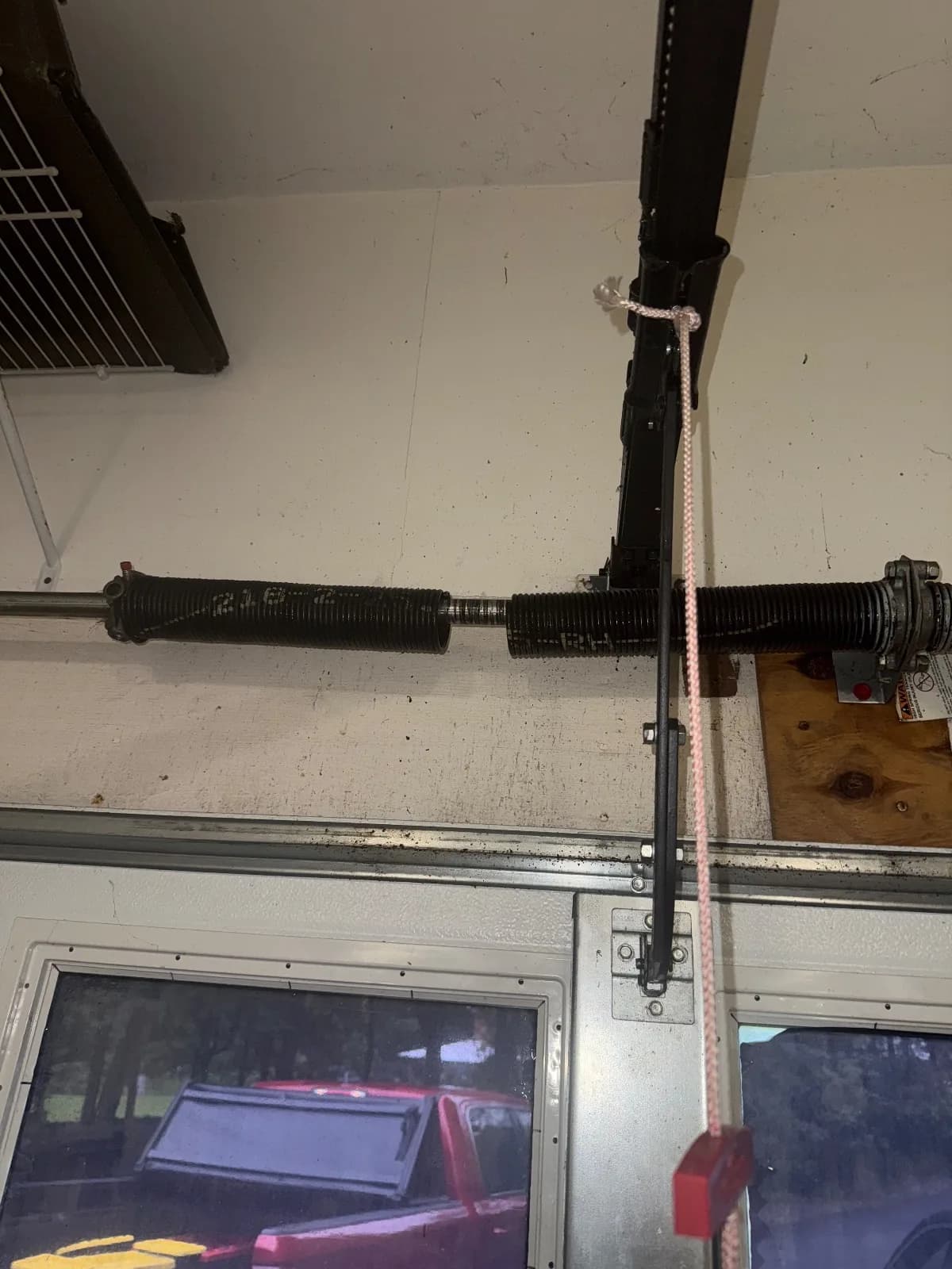 Close-up view of a broken black garage door torsion spring showing a gap in the coiled metal on the torsion bar.