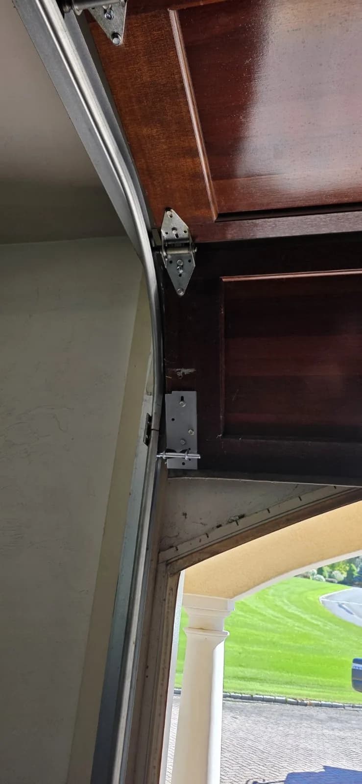 Inside view of a wooden garage door panel featuring a newly installed steel bottom bracket and roller mounted along the vertical track.