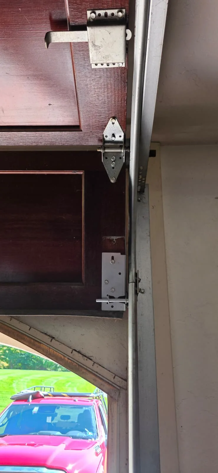 Interior view of the garage door section with a new bottom bracket, metal roller stem, and hinge attached to the door frame.
