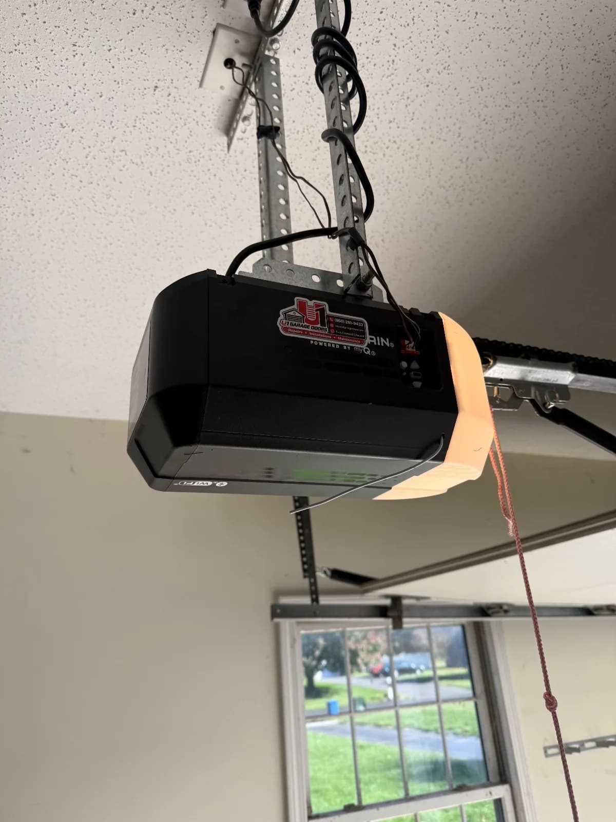 A black Chamberlain garage door opener motor unit mounted to perforated metal ceiling straps in a garage.