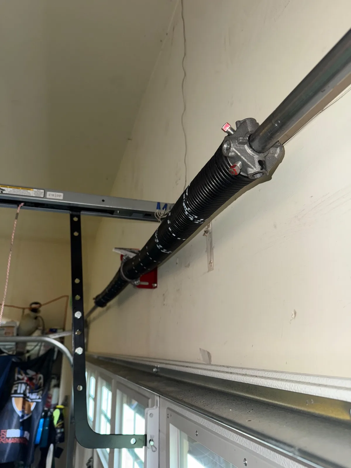 A garage door torsion spring with white winding marks mounted on a steel shaft above the garage door.