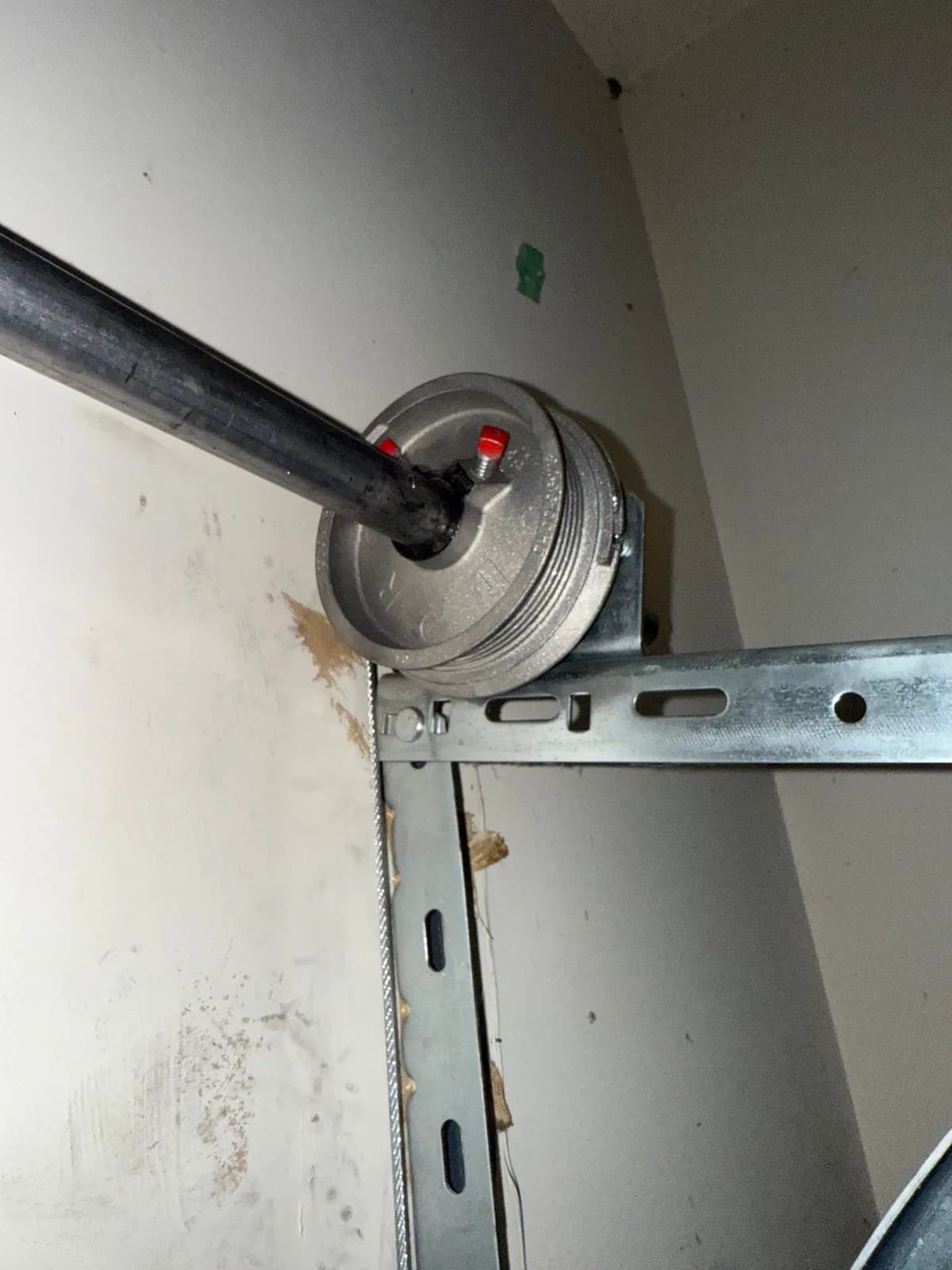 Close-up view of a metal cable drum and lift cable attached to a garage door shaft bracket.