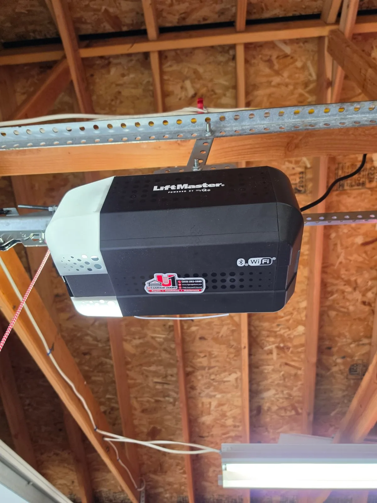 LiftMaster garage door opener motor unit mounted to exposed wooden ceiling framing inside a garage.