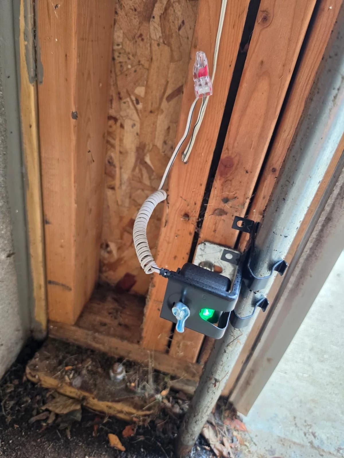 Safety sensor mounted on a metal garage door track showing an active green indicator light.