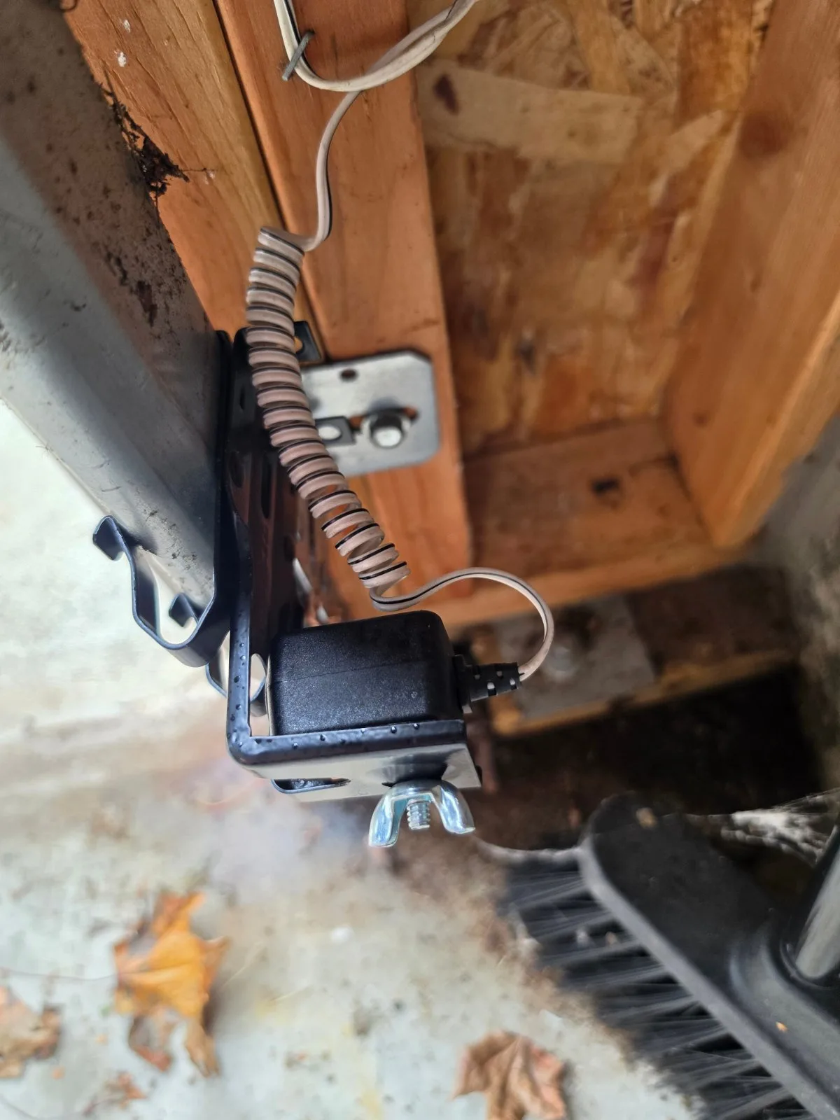 Black garage door safety sensor attached to the track assembly near the concrete floor.