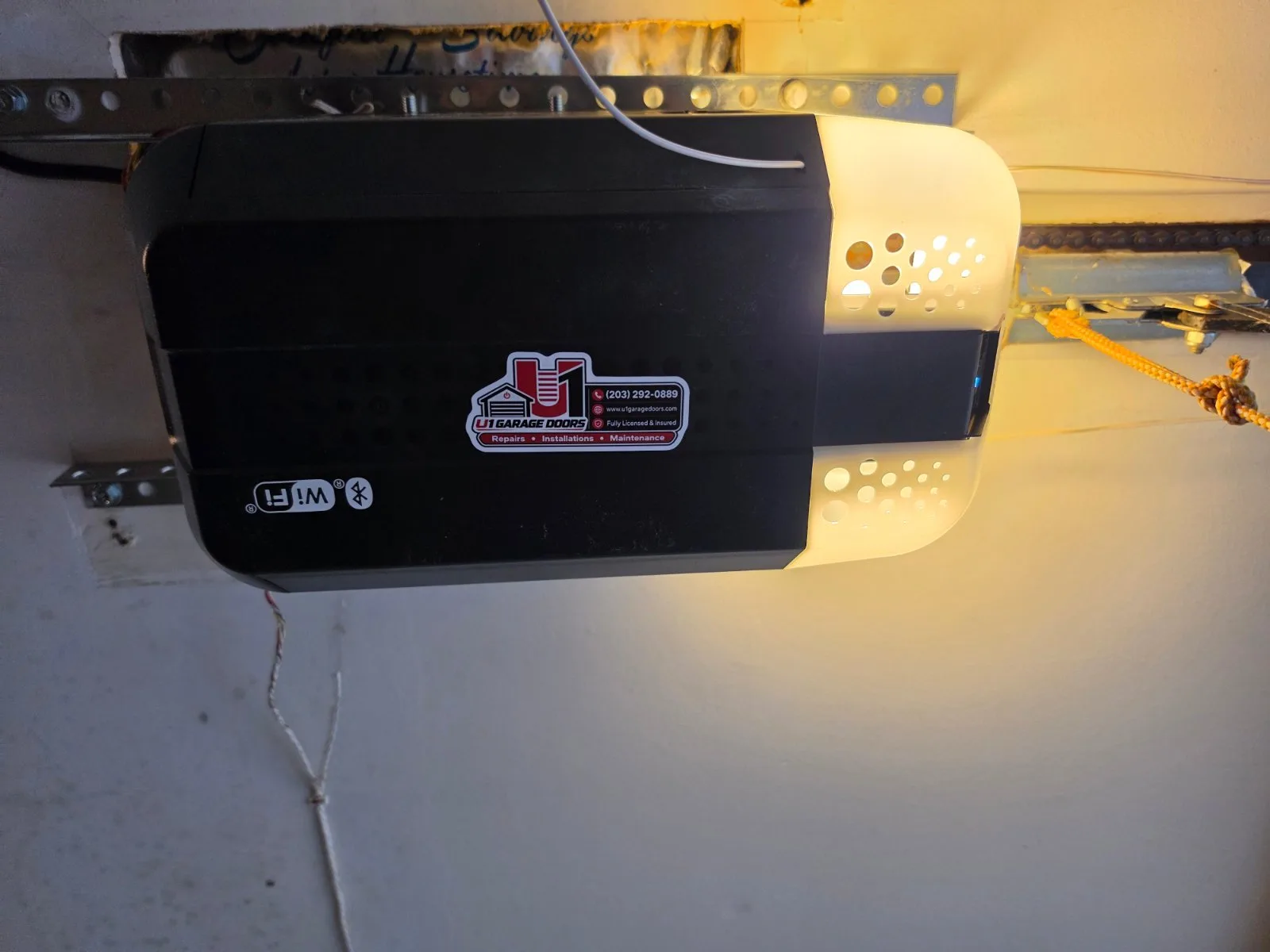 A black and white LiftMaster garage door opener unit installed on the garage ceiling with its light turned on.