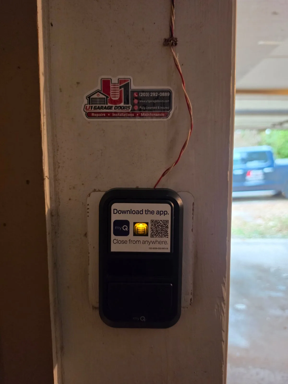 A black LiftMaster myQ wall-mounted garage door opener control console attached to a wooden frame.
