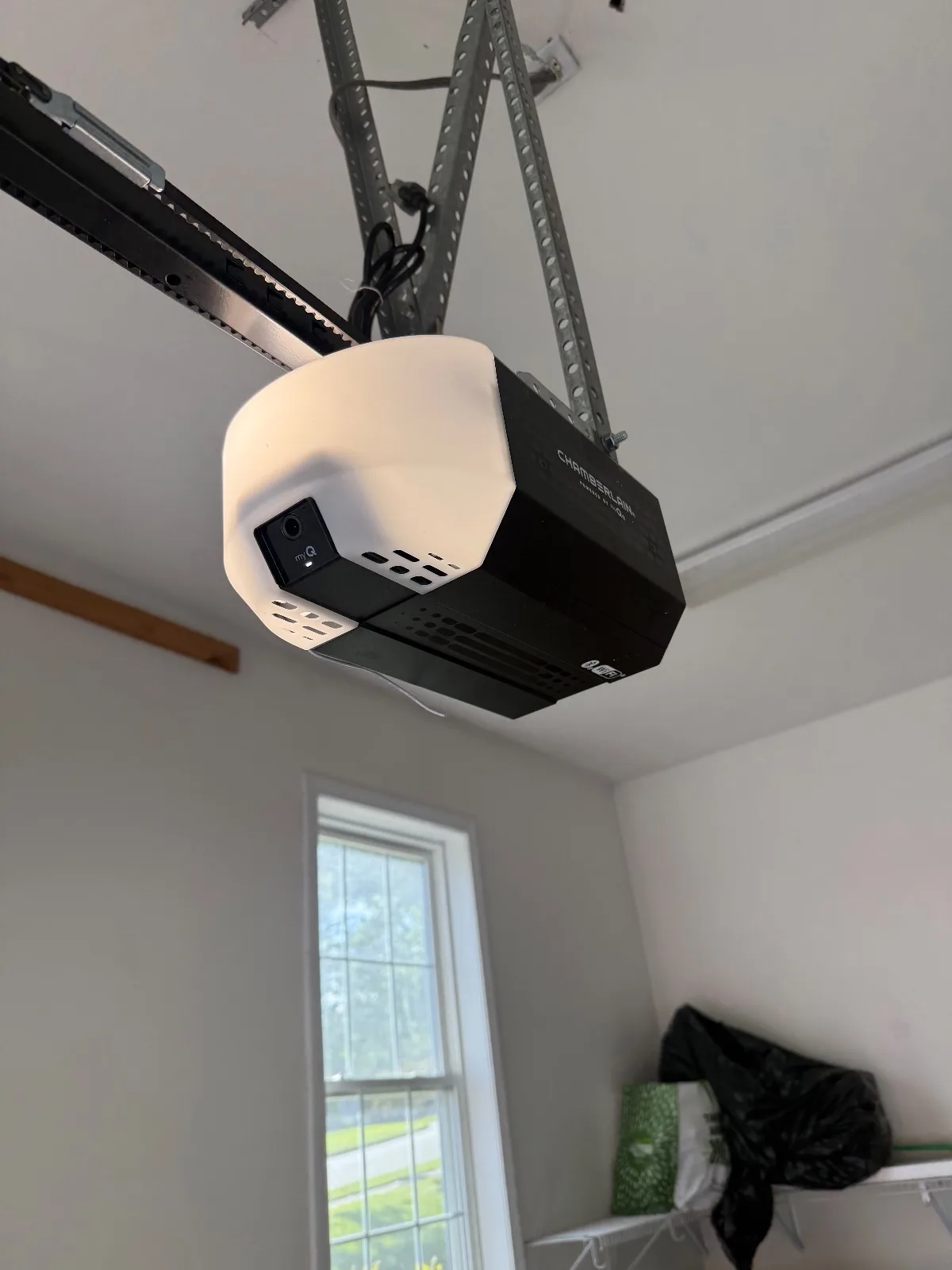 A black and white Chamberlain smart garage door opener mounted on metal ceiling support brackets inside a garage.