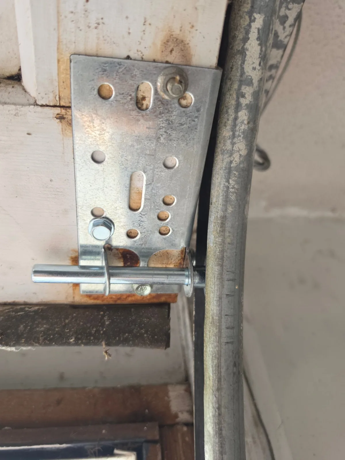 A clean metal bottom bracket and roller stem installed on the corner of a garage door panel next to a track.