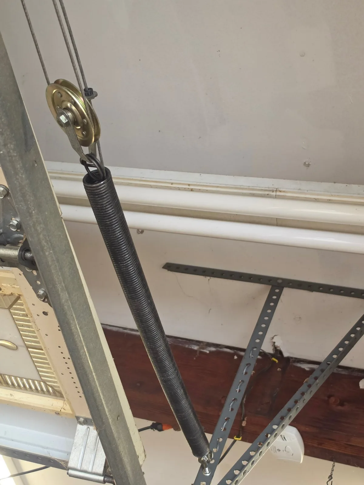 A newly installed black garage door extension spring attached to a pulley and cable along metal tracks.