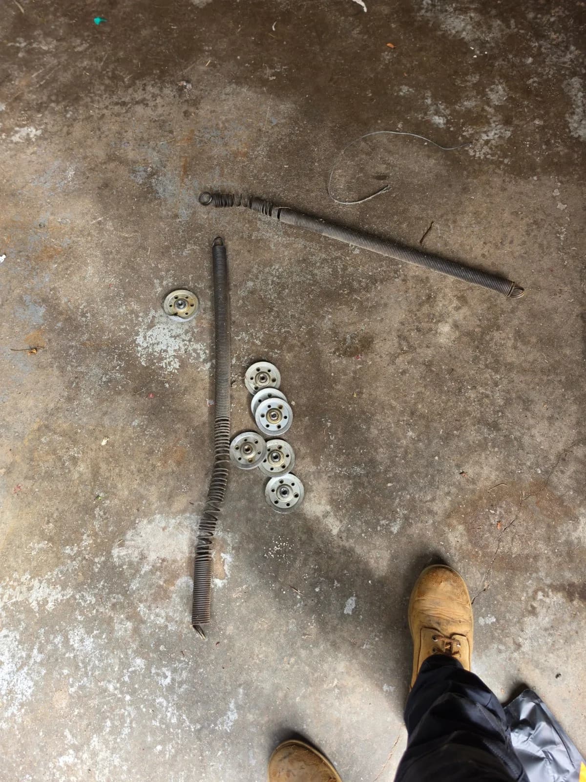 Old damaged garage door extension springs and several worn pulleys lying on a concrete garage floor.