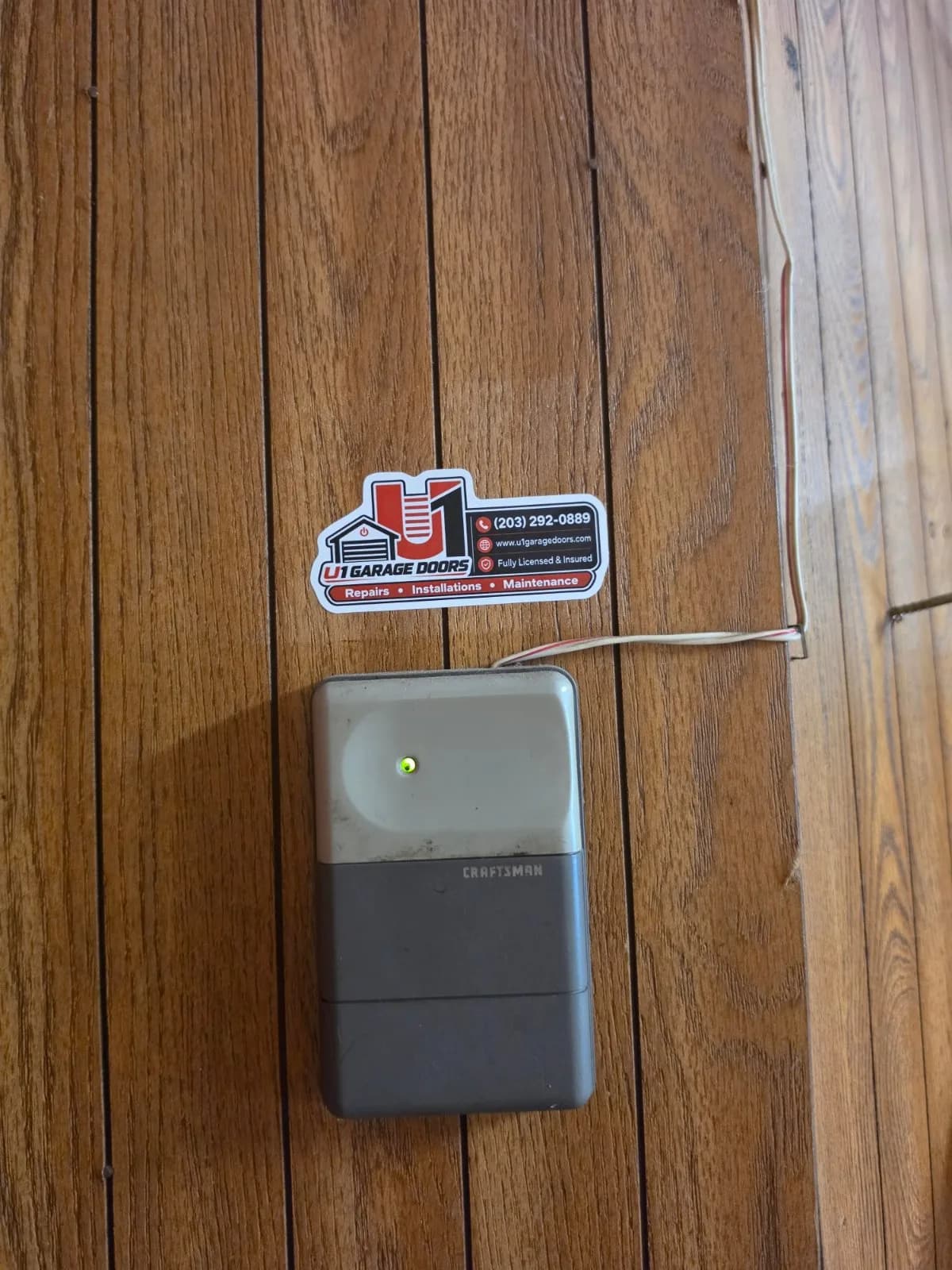 A grey Craftsman garage door opener wall console with a green light on wood paneling.